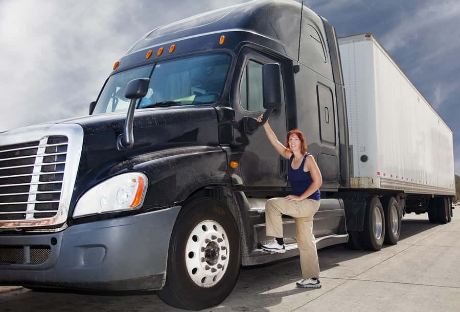 Woman with her hand on a semi-truck mirror posing for a picture
