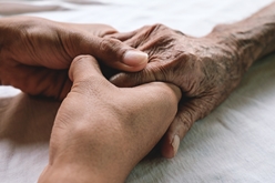 family holding the hands of their elderly relative in a nursing home