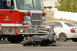 motorcycle laying on the road next to a firetruck after a motorcycle accident