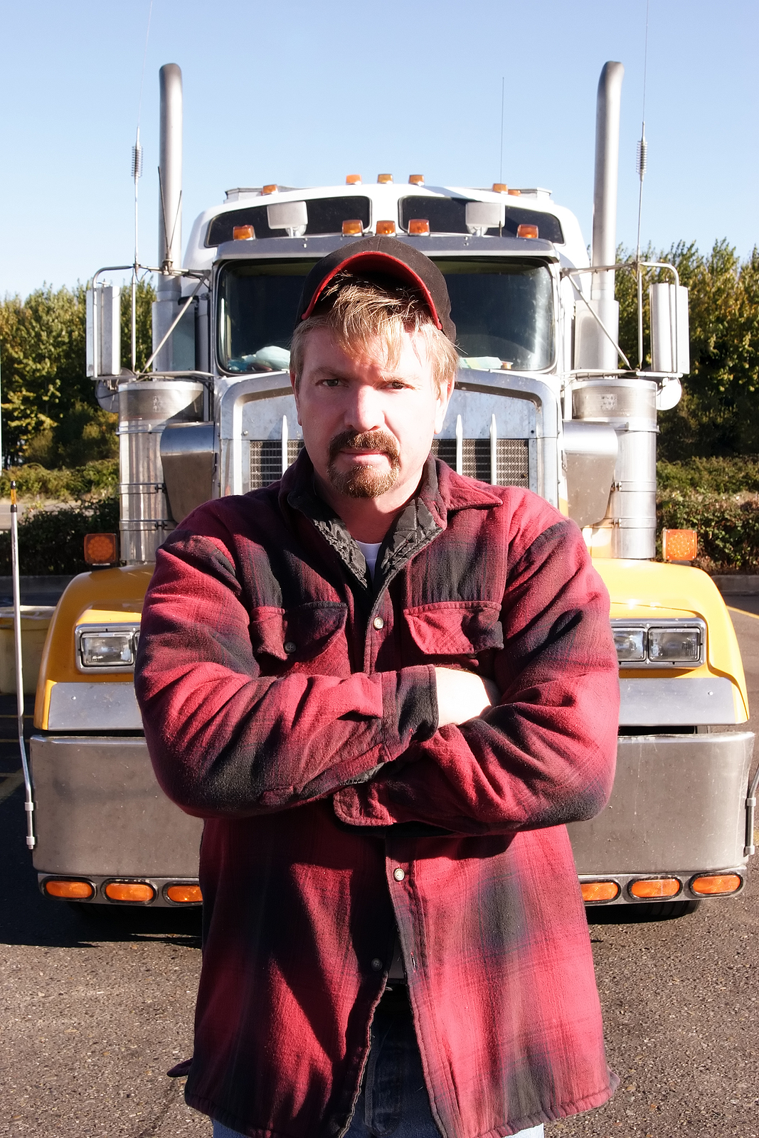 Semi truck driver posing with arms crossed in front of truck