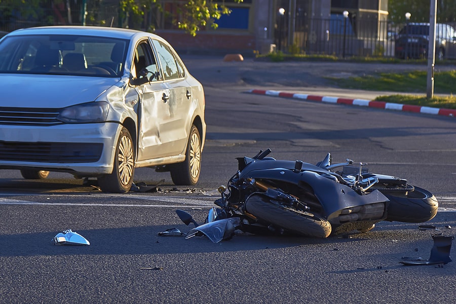 Motorcycle wrecked on the road next to a damaged silver car