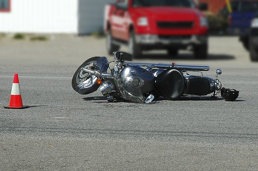 black motorcycle layed out on the road with safety cones surrounding the accident