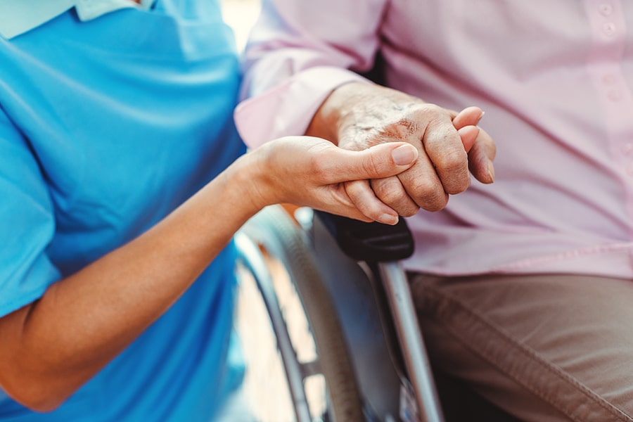 elderly person holding the hand of nursing home caretaker