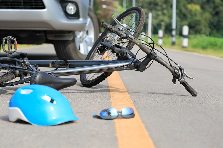 bicycle hit by a silver car or truck with blue helmet and glasses on the ground next to it