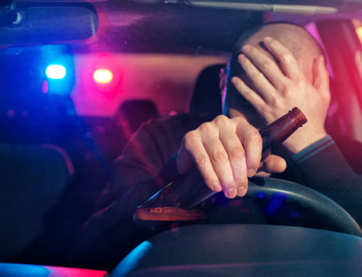 Driver with an alcohol bottle in hand being stopped by a police car