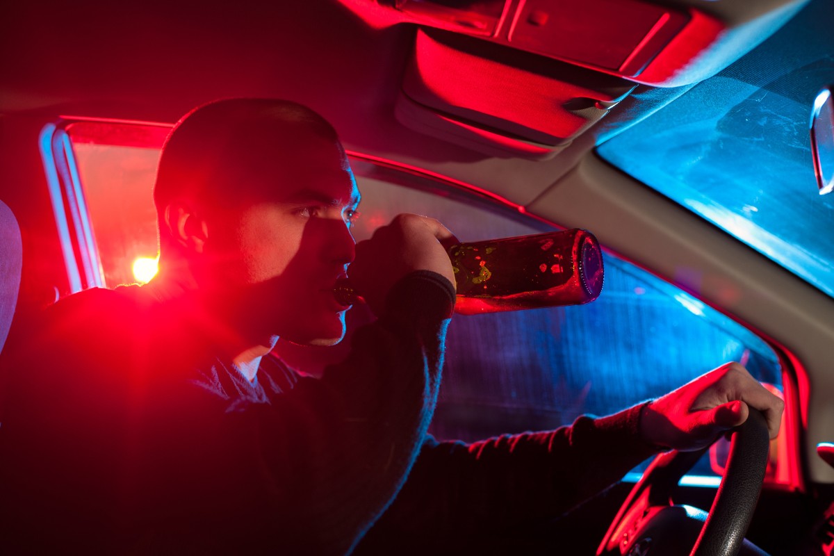 Man driving a car while drinking beer as a police car approaches