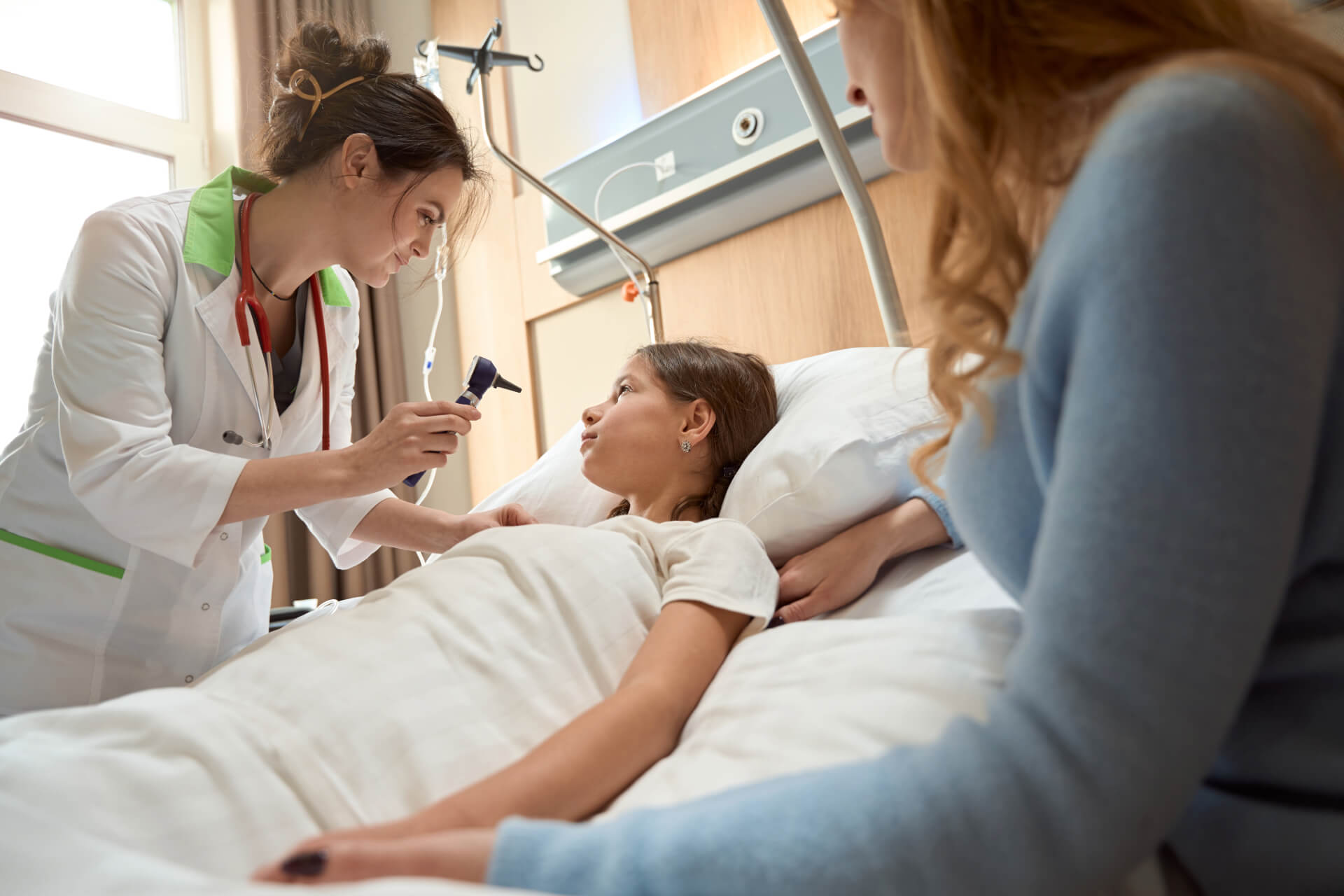 doctor holding stethoscope up to child in hospital bed