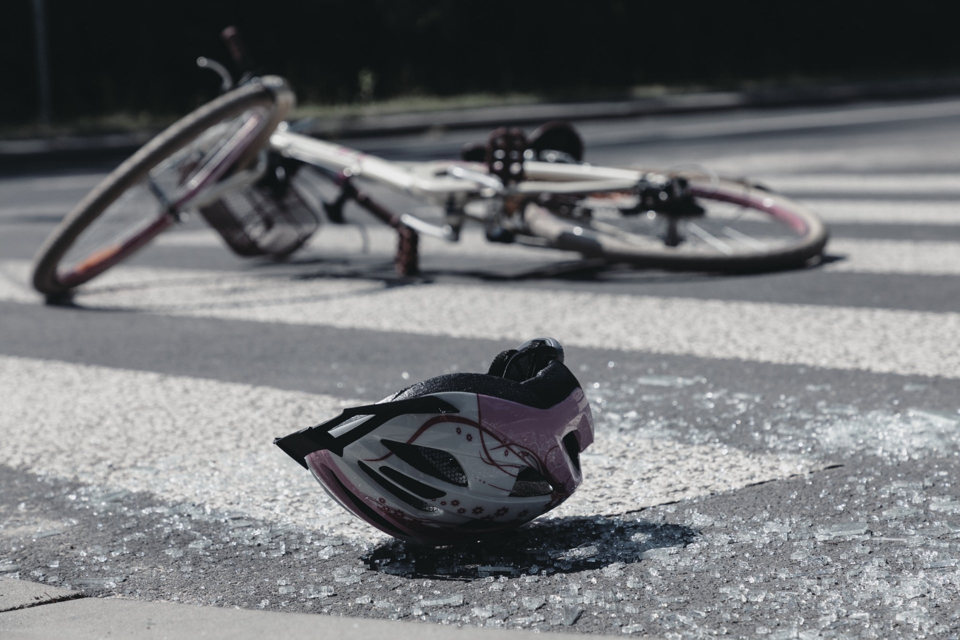 Crashed helmet and bike lying on a crosswalk with shattered glass