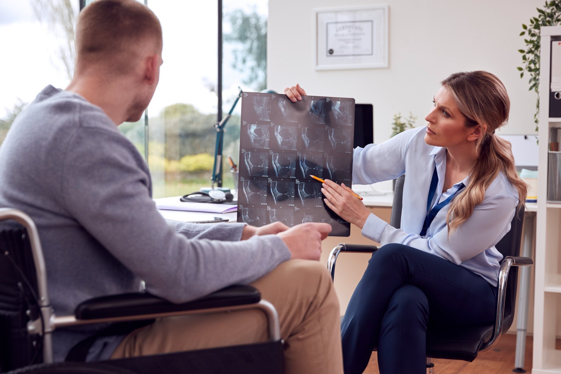 Doctor showing a knee X-ray to a male patient in a wheelchair