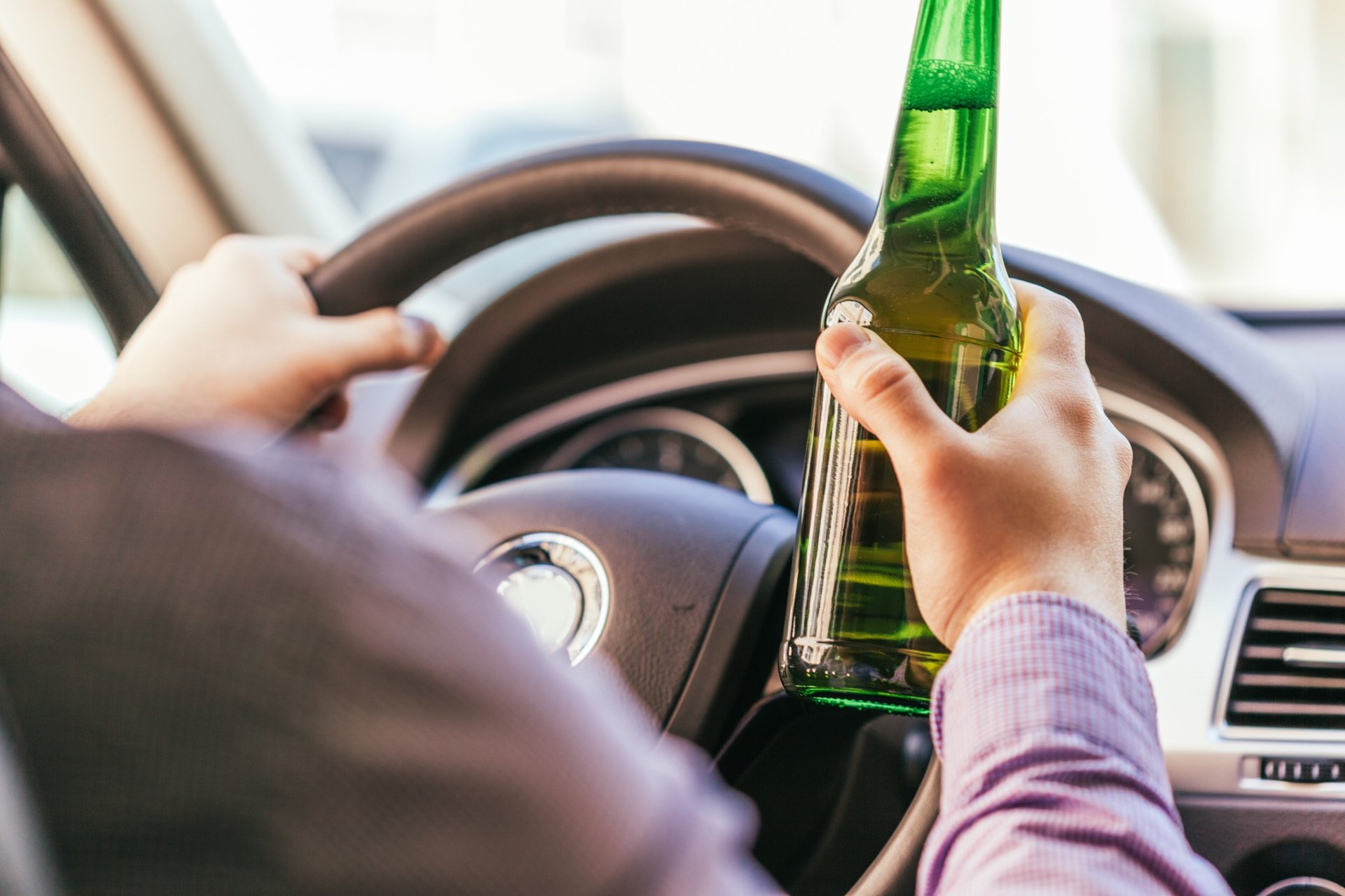 Driver holding a green beer bottle behind the wheel