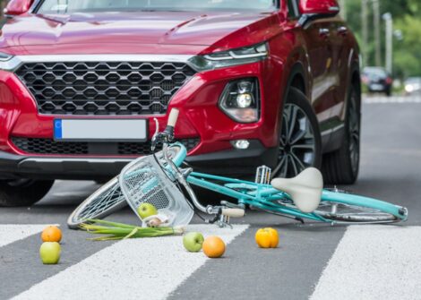 Groceries spilled and a bicycle hit by a red SUV at a crosswalk