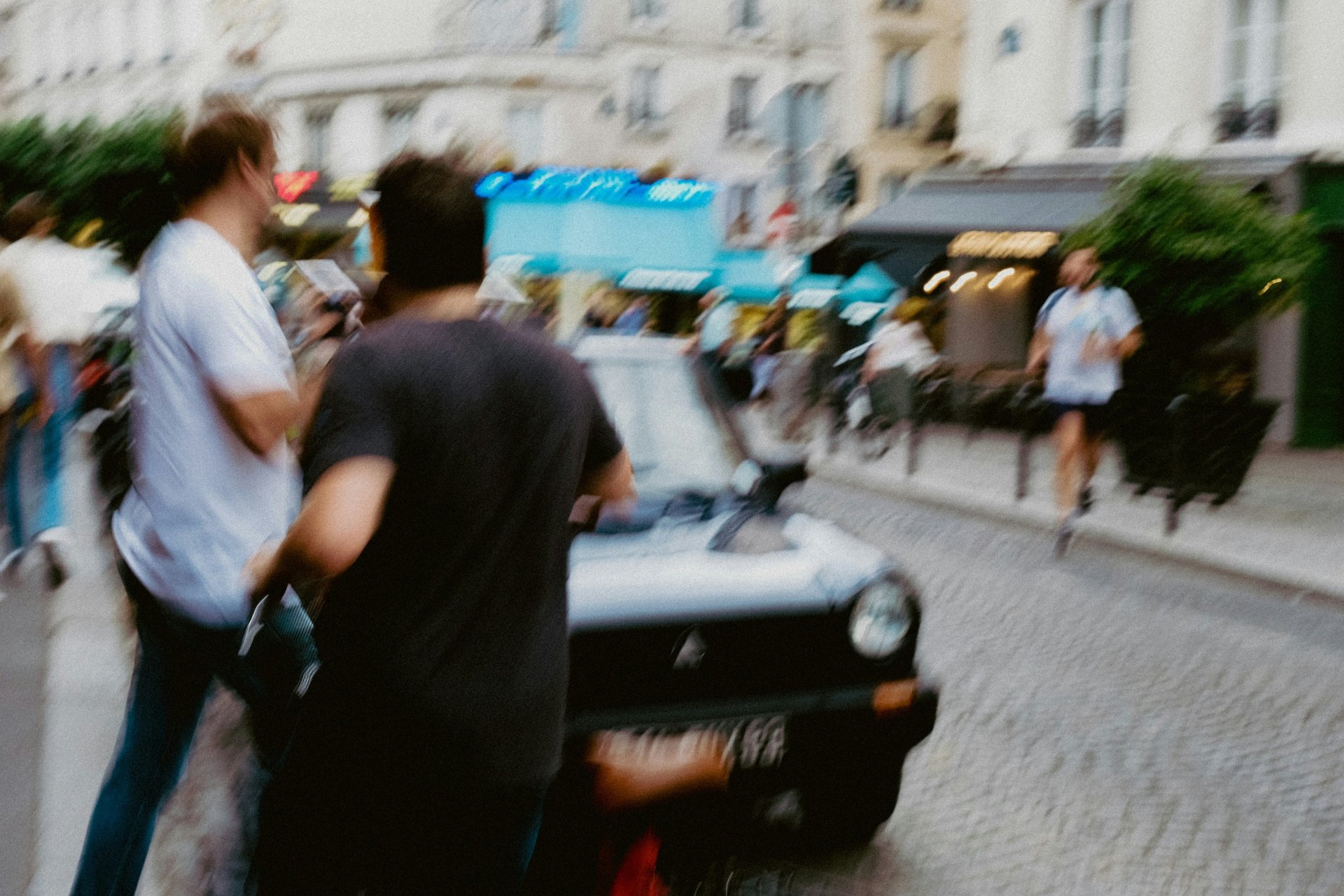 Blurred image of people on a street near a vintage car, possibly after an incident