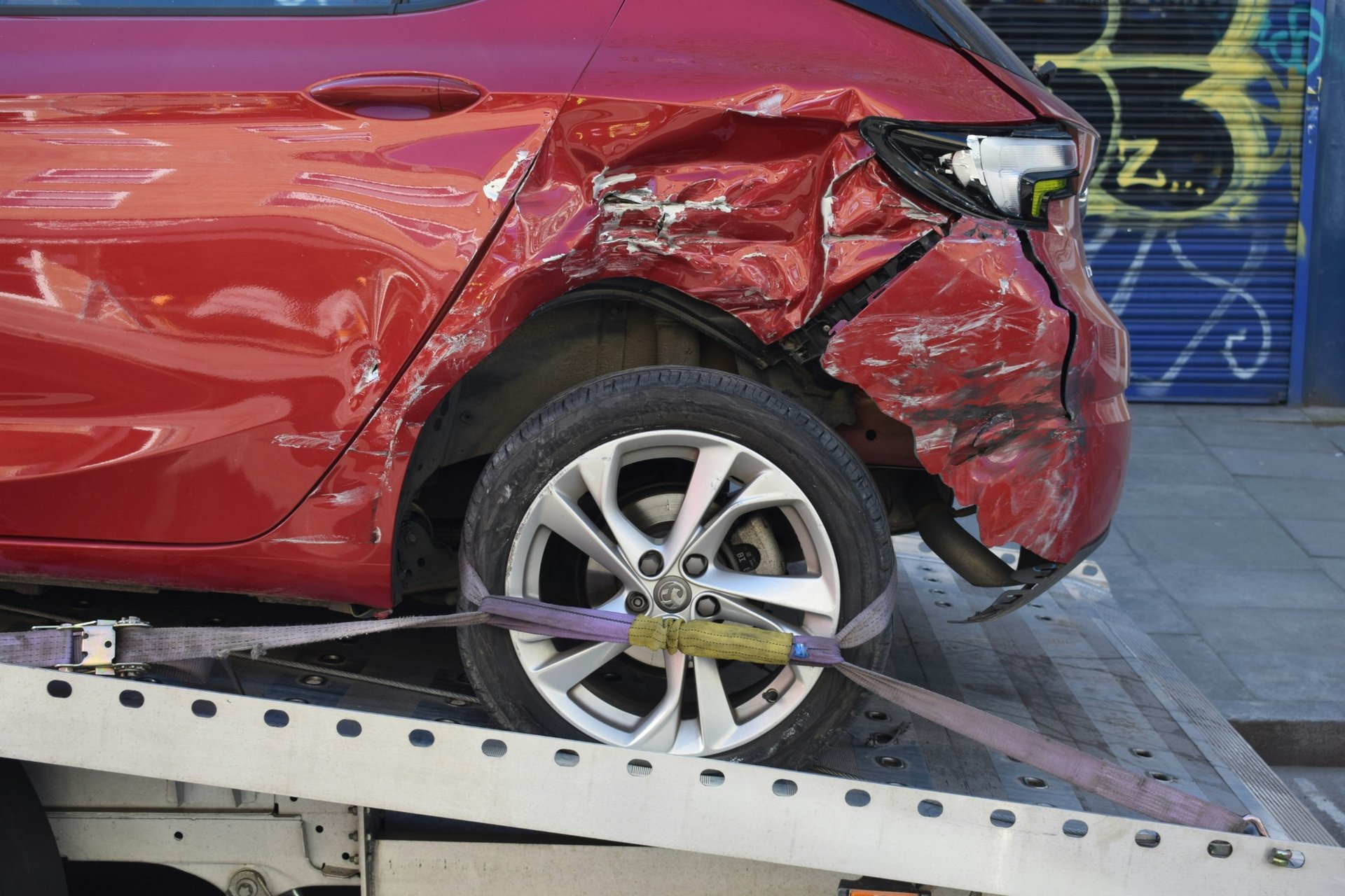 Heavily damaged rear side of a red car secured on a tow truck